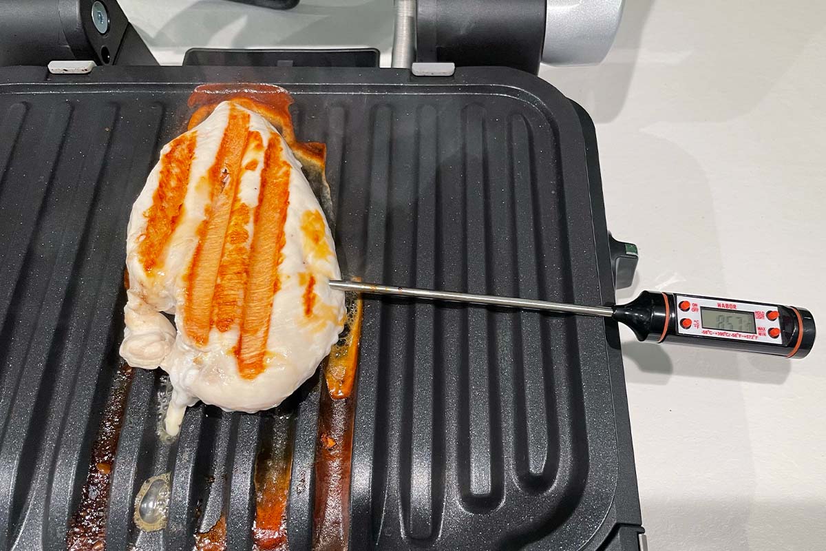 Ein gegrilltes Stück Geflügelbrust auf der Garplatte des Tefal-Kontaktgrills mit Bratenthermometer.