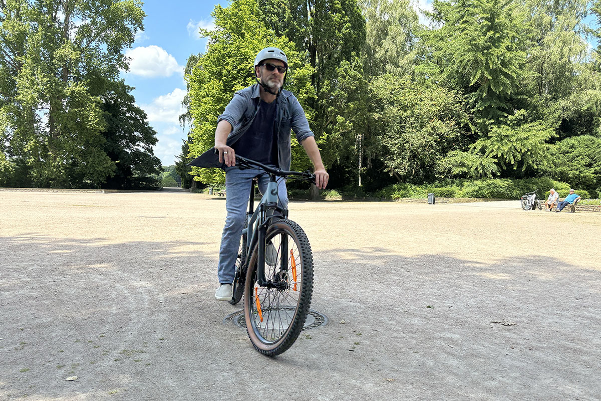 Mann fährt im Park auf einem E-Bike. Der Fahrer kommt direkt auf die Fotografin der Szenerie zu.