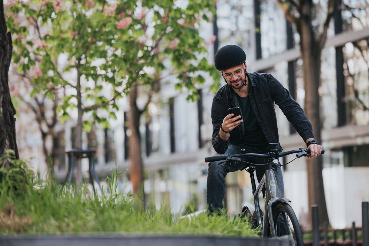 Mann sitzt auf seinem Rad, hat den einen Fuß auf einer Mauer gelehnt, er schaut in sein Smartphone