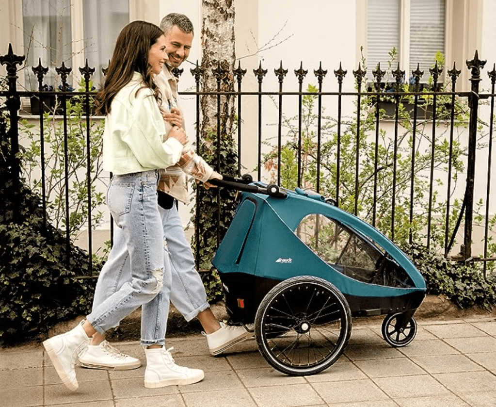 Ein Fahrradanhänger als Buggy auf dem Gehweg mit einer Frau und einem Mann. 