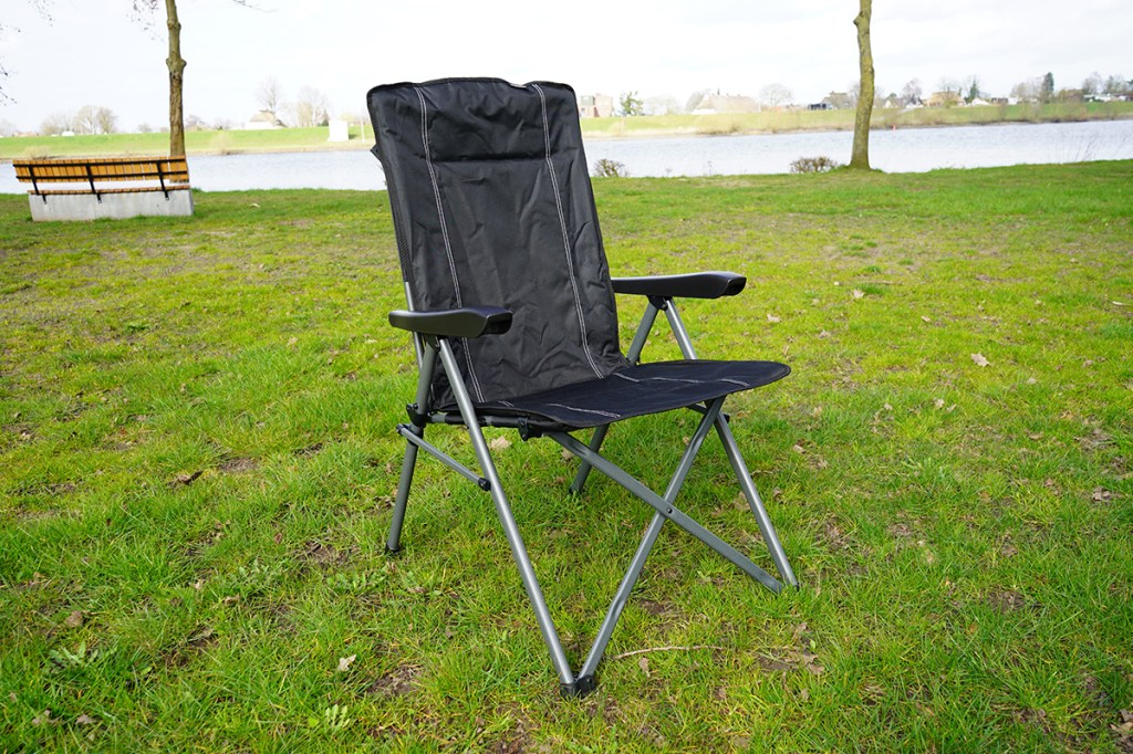 Der schwarze Campingstuhl von Dometic vor grüner Wiese und Fluss im Hintergrund.