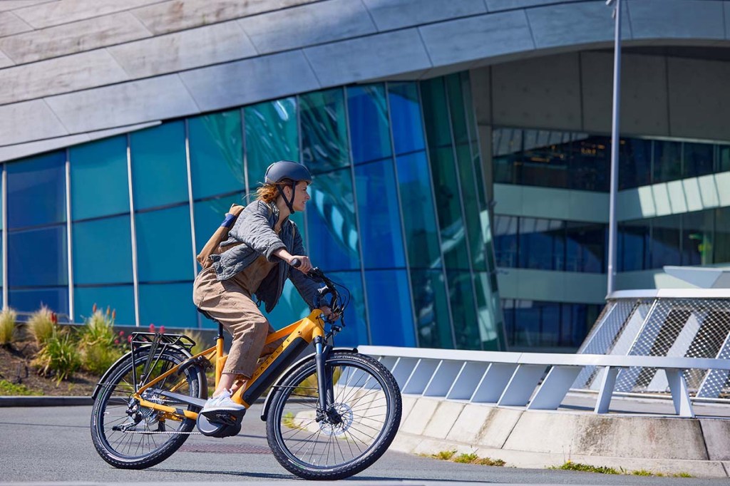 Frau fährt mit einem gelben E-Bike an einer Häuserfront vorbei