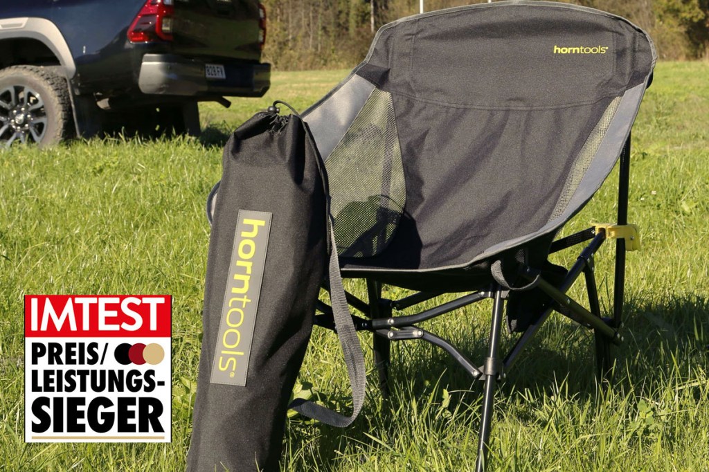 Der Campingstuhl "Explorer" von Horntools auf einer Wiese. Im Hintergrund ein schwarzes Offroad-Fahrzeug. Mit Preis-Leistungs-Sieger-Siegel von IMTEST.