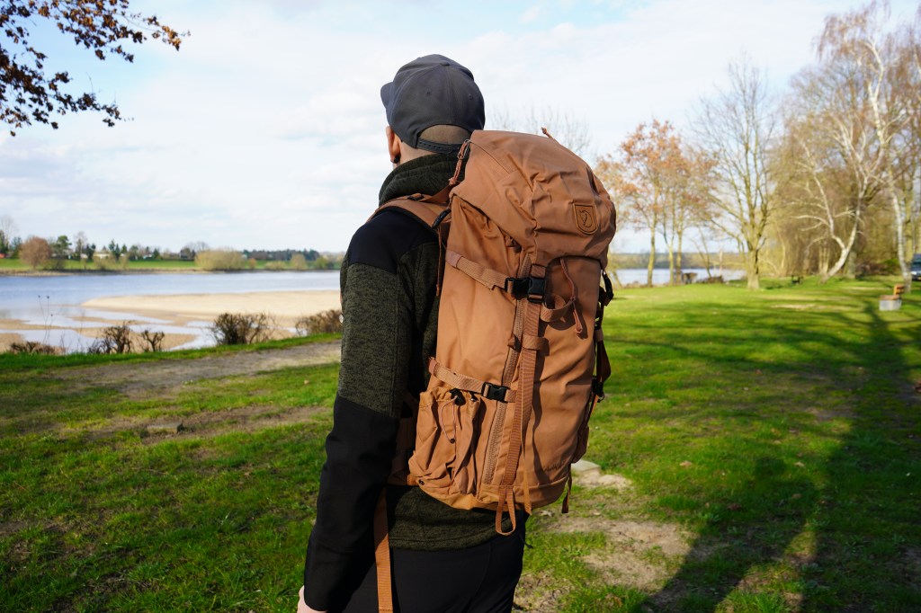 Mann von hinten in der NAtur, er hat einen großen Trekking-Rucksasck auf dem Rücken