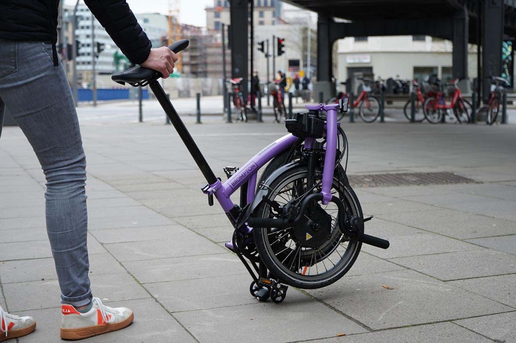 Nahaufnahme Person schiebt über die Sattelstange ein zusammgeklapptes Fahrrad