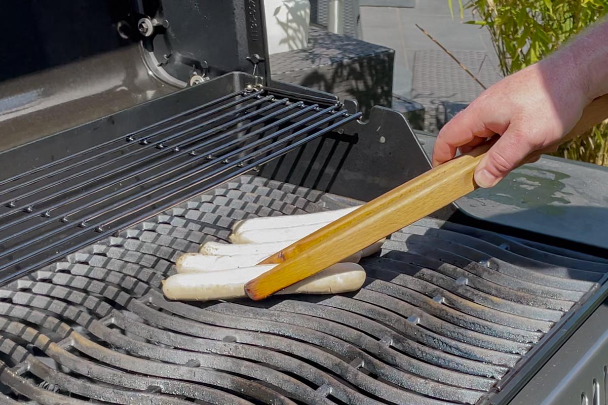 Bratwürste werden auf einen Gasgrill gelegt.