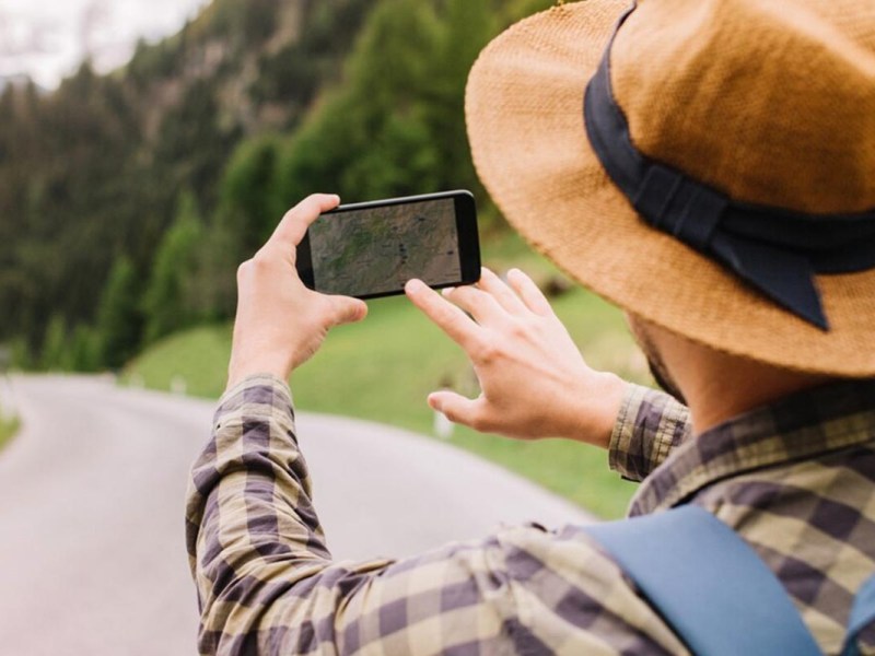 Person hält ein Smartphone in der Hand und steht auf Asphalt.