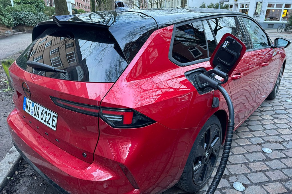 Detailansicht E-Auto an Ladesäule in städtischer Umgebung mit angeschlossenem Ladekabel schräg von hinten nach vor fotogrfiert.