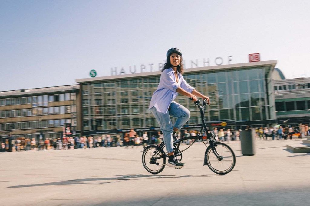 Frau fährt auf einem Faltrad auf dem Platz vorm Kölner Hauptbahnhof