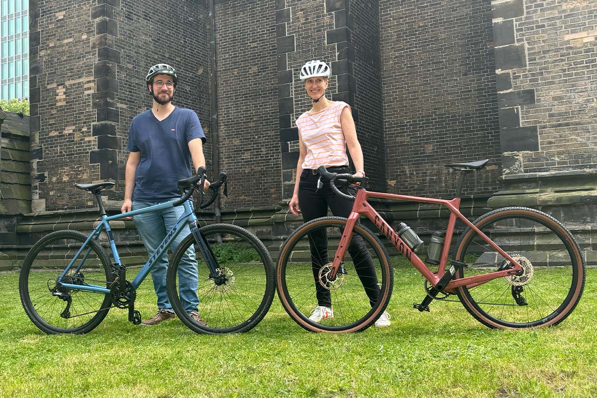 Zwei Gravelbikes stehen sich gegenüber,die jeweils von einer Person, die hinterm Rad steht, festgehalten wird