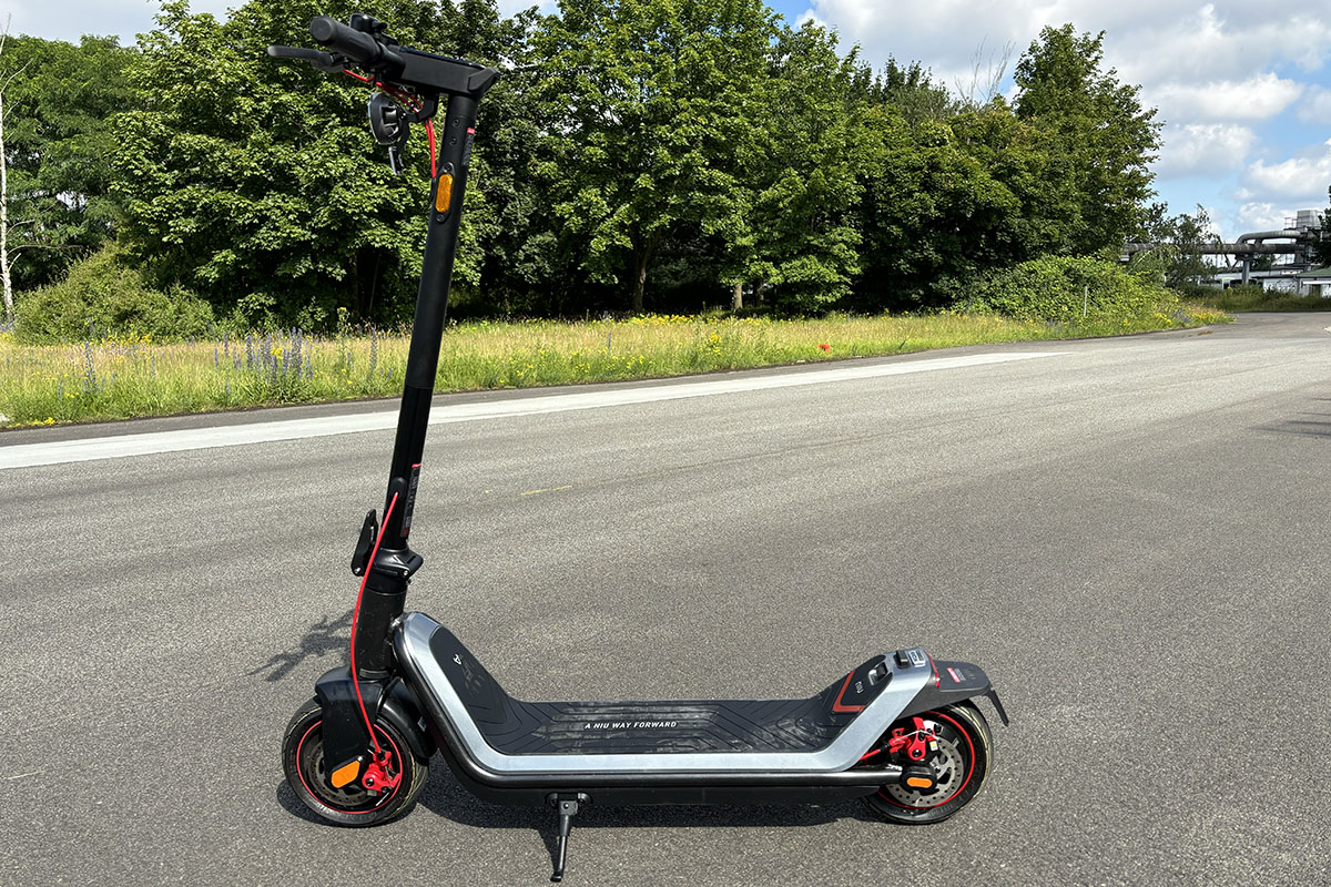 E-Scooter steht im Profil auf Straße vor Waldstück.