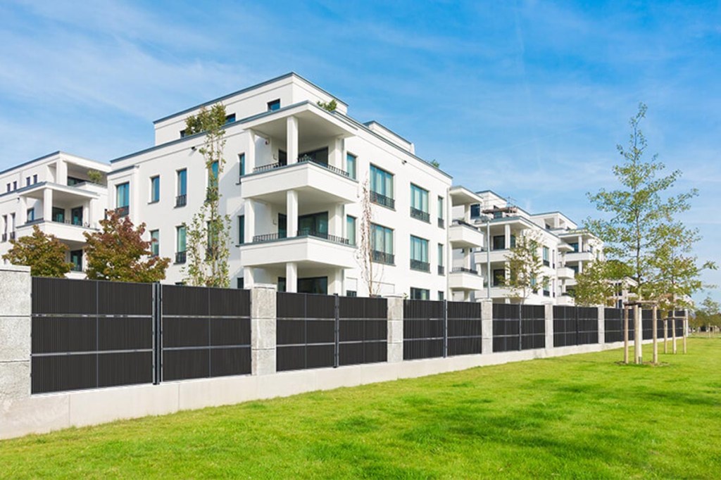 Ein weißes Wohnhaus mit grünem Rasen und einem Solar-Zaun davor.