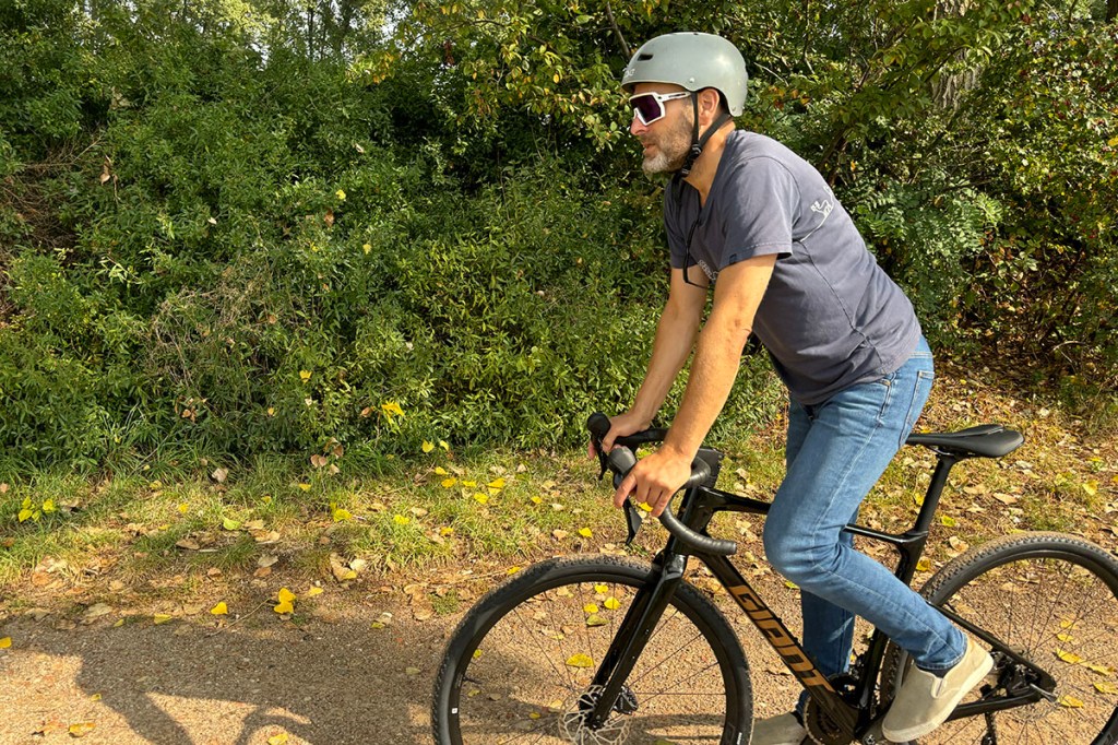 Mann fährt im Stehen auf einem Gravelbike durch Parklandschaft.