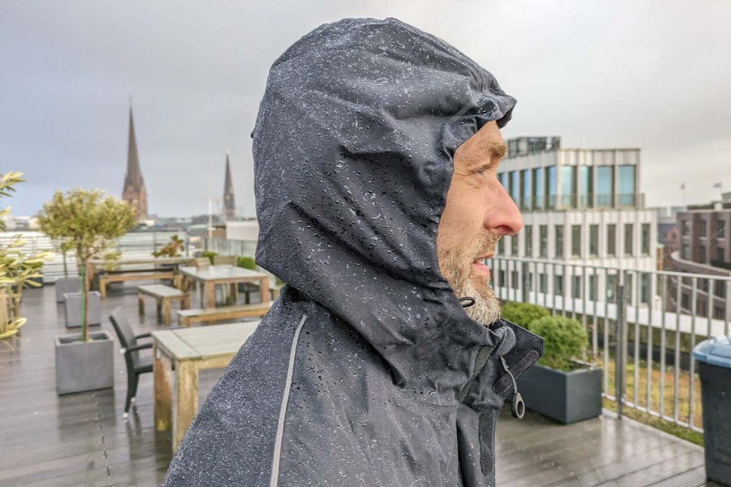 Person nah von der Seite, hat eine schwarze Regenjacke mit Kaputze auf