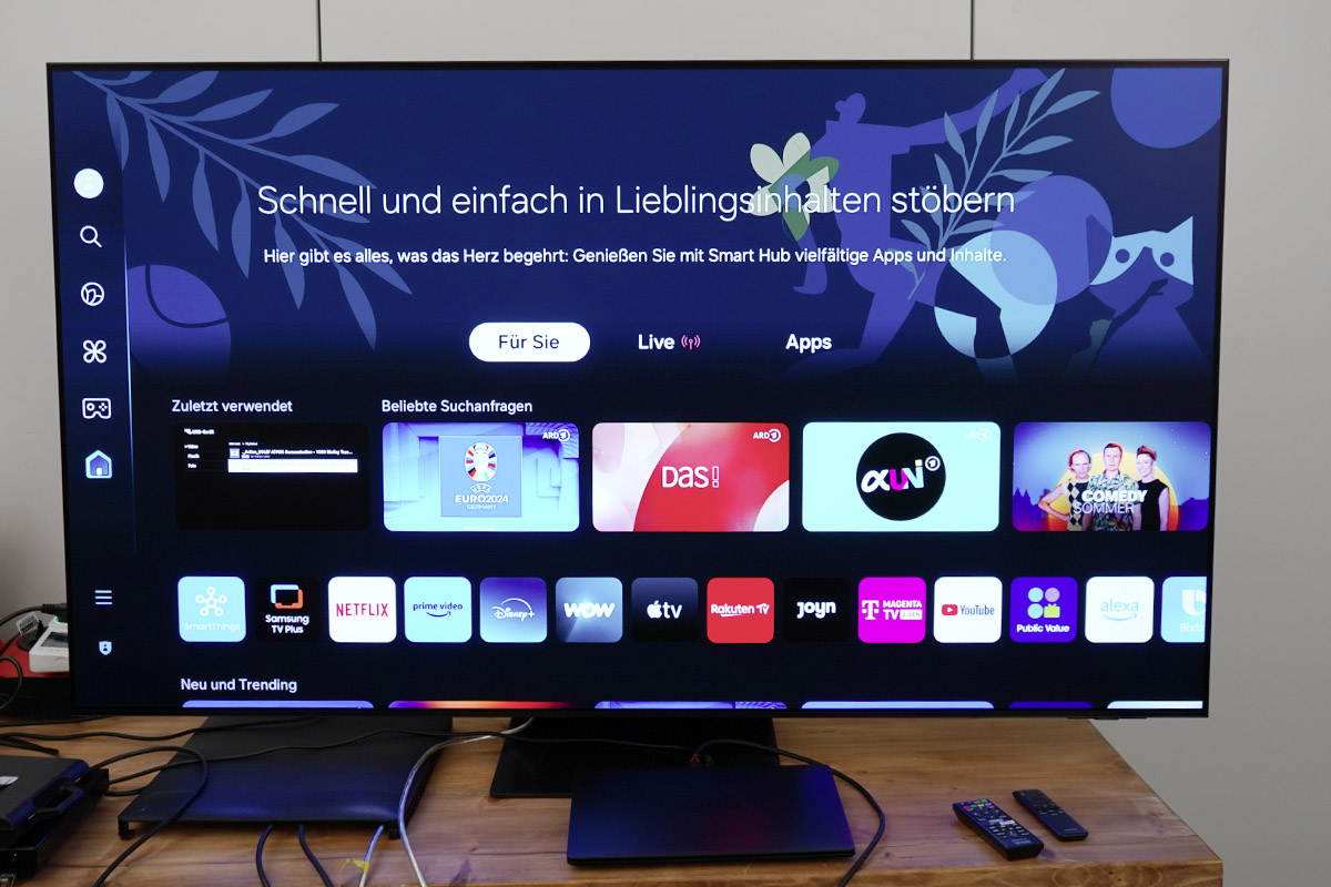 Ein Smart-TV Samsung Galaxy S95D steht eingeschaltet auf einem Holztisch.