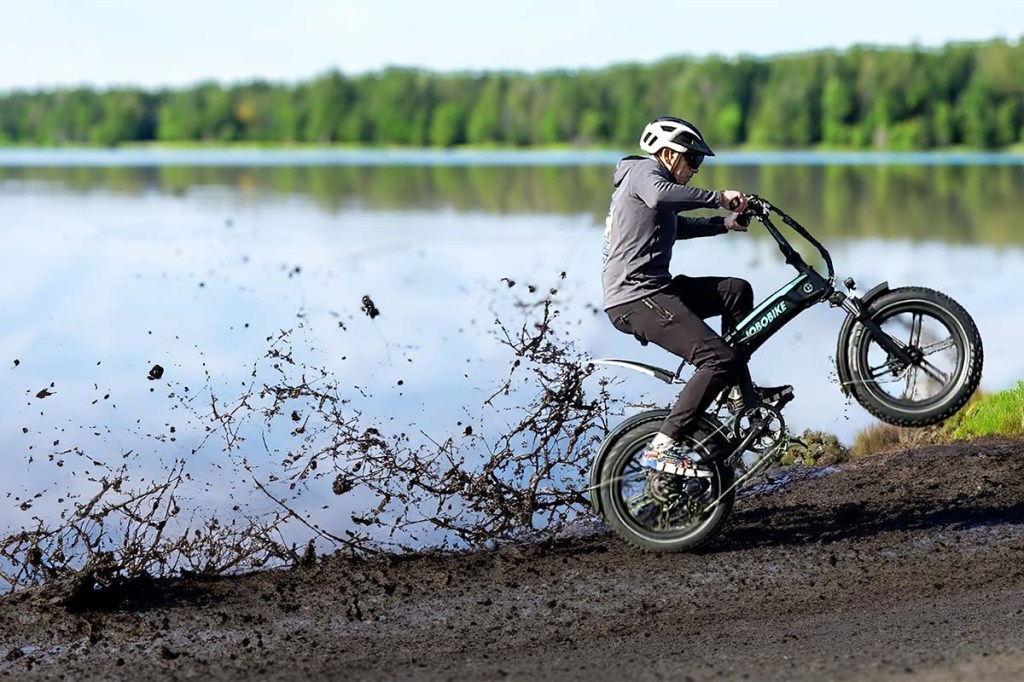 Person mit einem Fat-E-Bike mit hochgezogenem Vorderrad, fährt durch Matsch