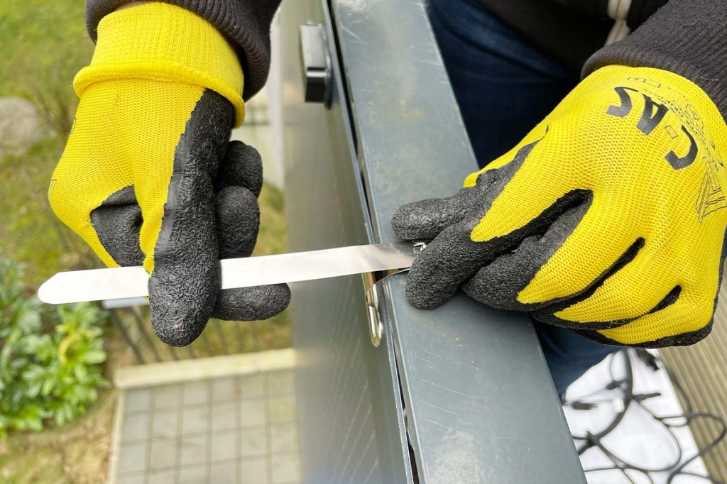 Eine Person mit gelben Handschuhen macht ein Solarpanel mit Kabelbindern an einem Geländer fest.