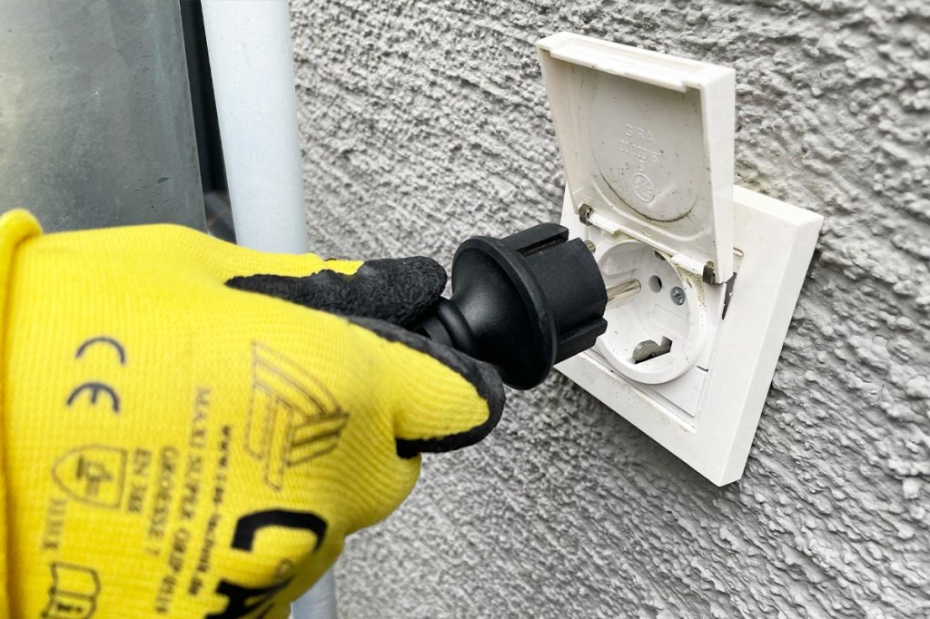 Eine Person steckt einen Schuko-Stecker in eine Außensteckdose.