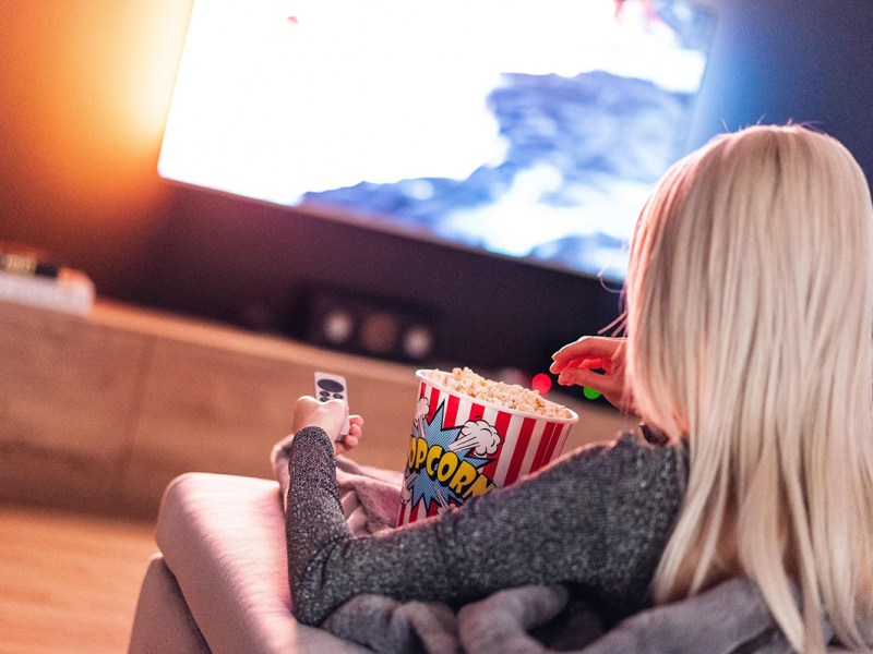 Blick über die Schulter einer Fernsehzuschauerin, die gerade Popcorn isst und das Programm genießt