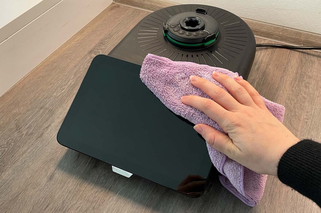 Eine Hand wischt das Thermomix-Grundgerät des TM7 mit einem lila Tuch ab.