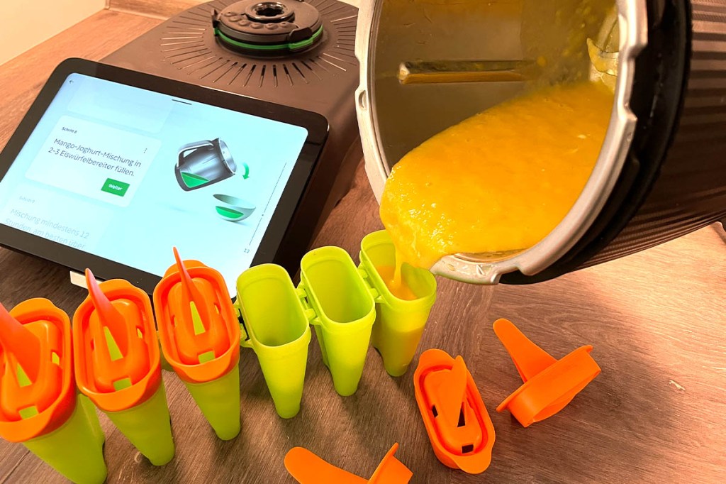Eine gelb-orangene Flüssigkeit wird vom Thermomix TM7 Mixtopf in Stiel-Eis-Formen gegossen.