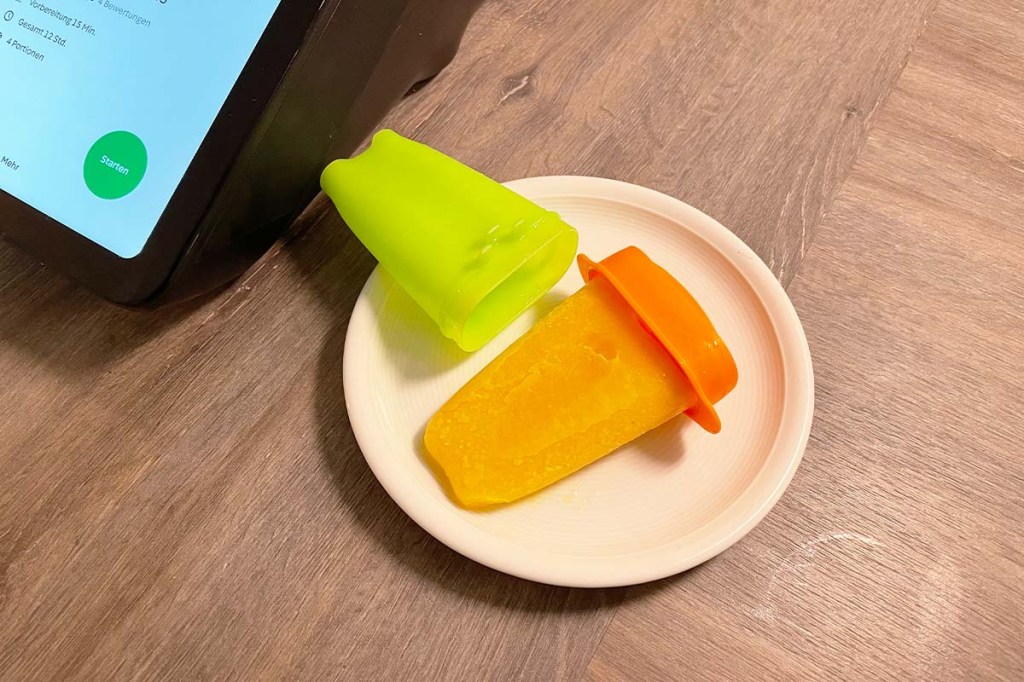 Ein selbstgemachtes, orangefarbenes Eis am Stiel neben dem Thermomix TM7